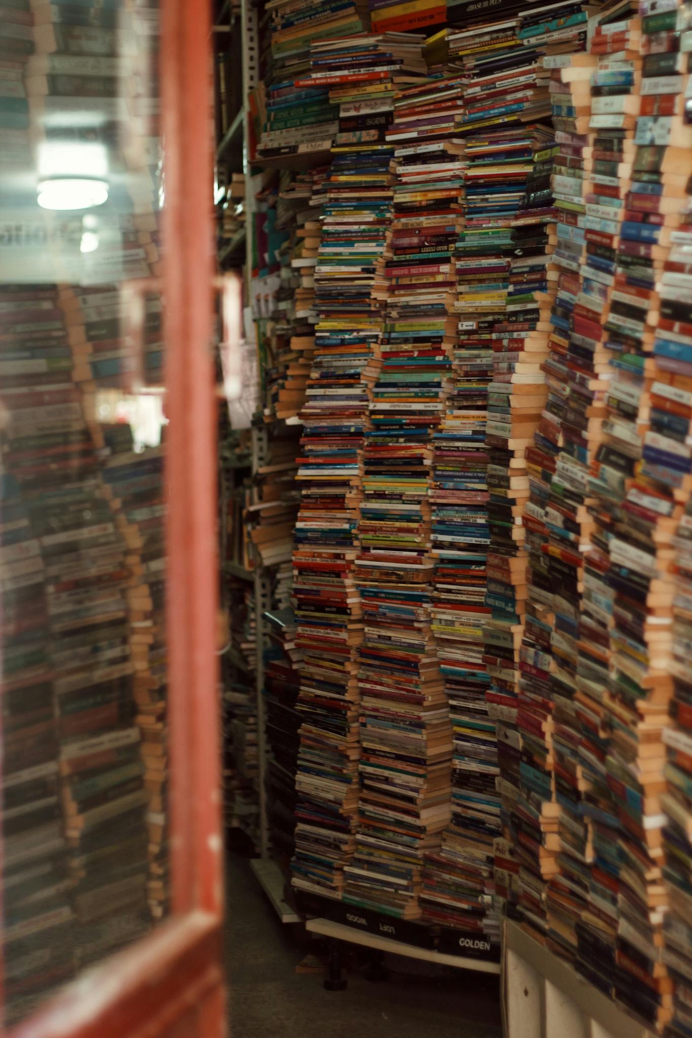 A cluttered bookshop features towering stacks of used books, visible through an open door.